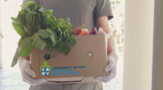 gloved hands carrying a cardboard box of fresh produce