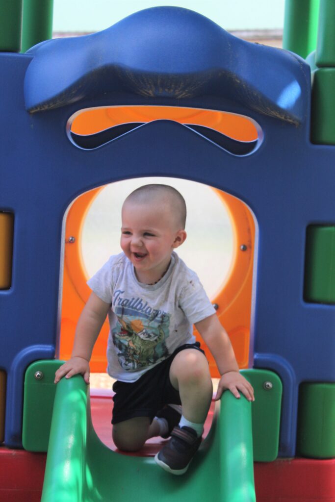 A toddler smiling at the top of a slide