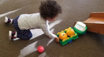Toddler pushing a toy truck with small pumpkins in the back