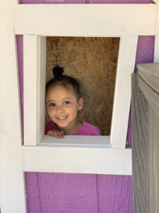 Preschool girl smiling out of the window of a play structure